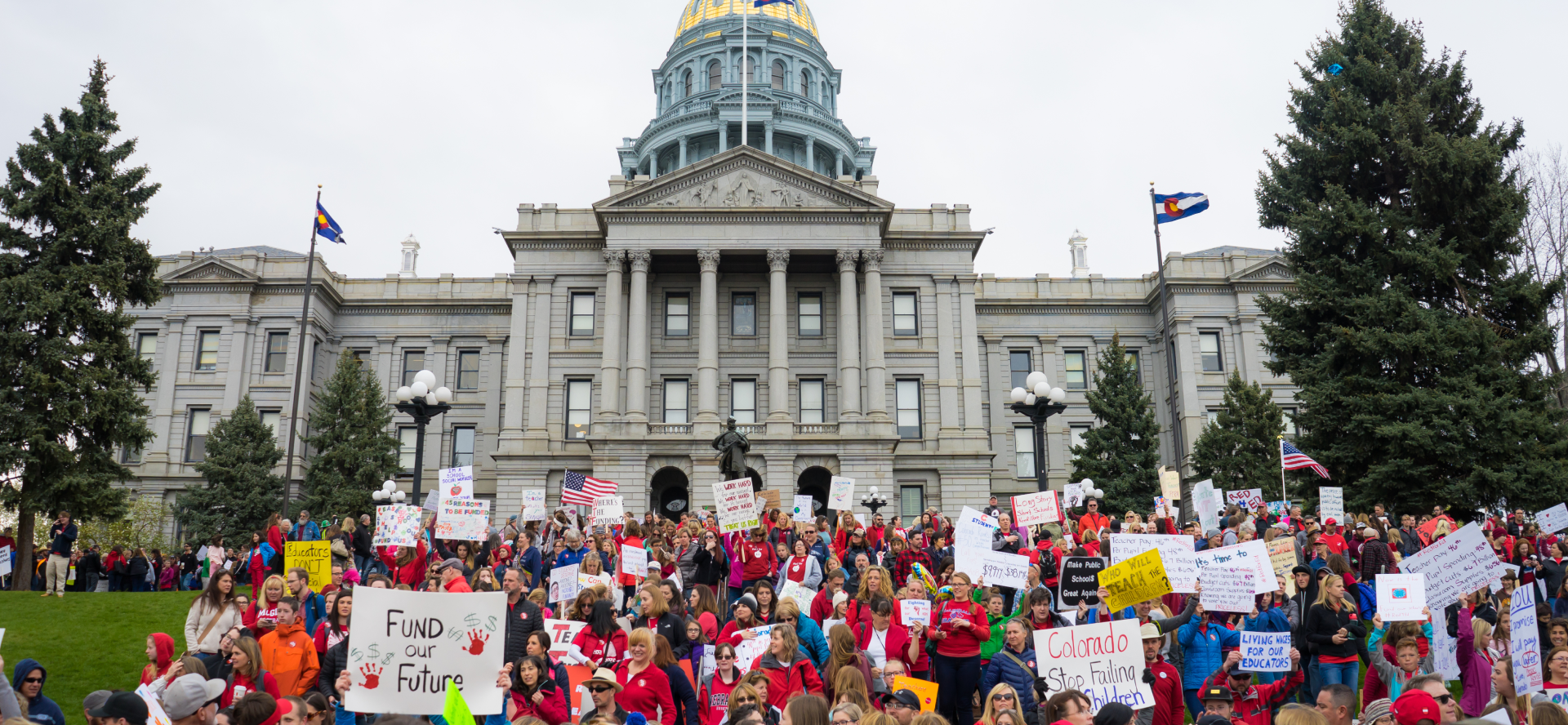 Colorado Education Association members rally in front of the Colorado state capitol building wearing red and carrying signs and banners